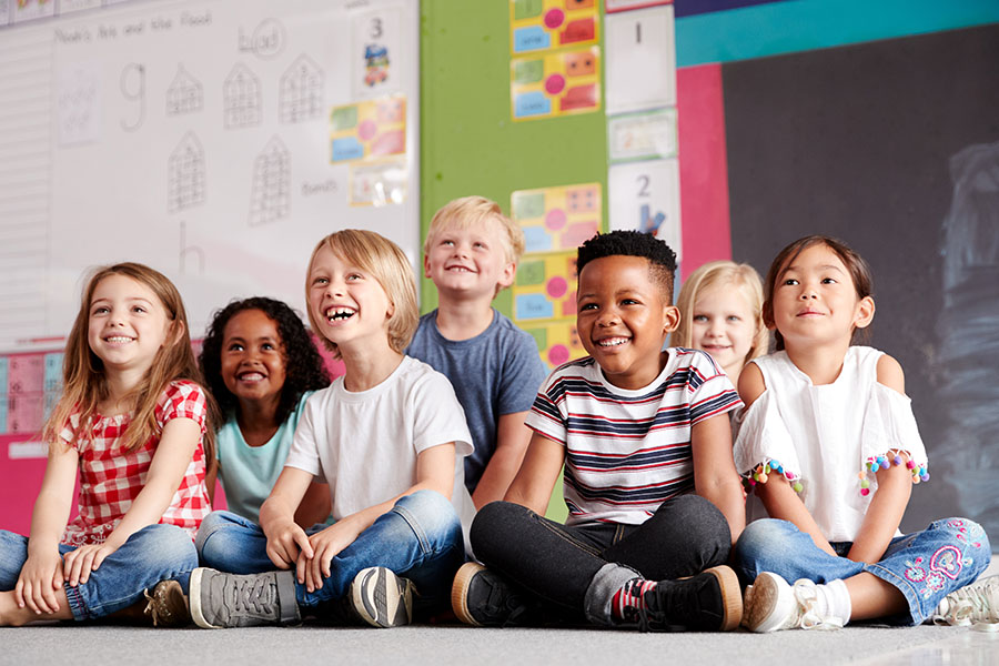 Specialized Business Insurance - View of Group of Smiling Diverse Children Sitting on the Floor in the Classroom