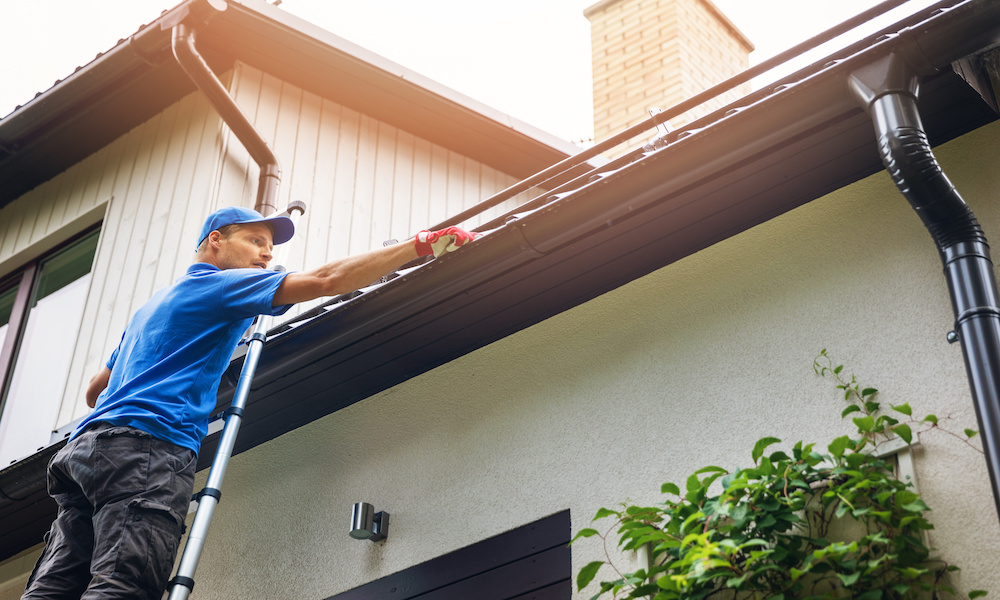 Tips for Fall Home Maintenance blog-man on ladder cleaning gutter