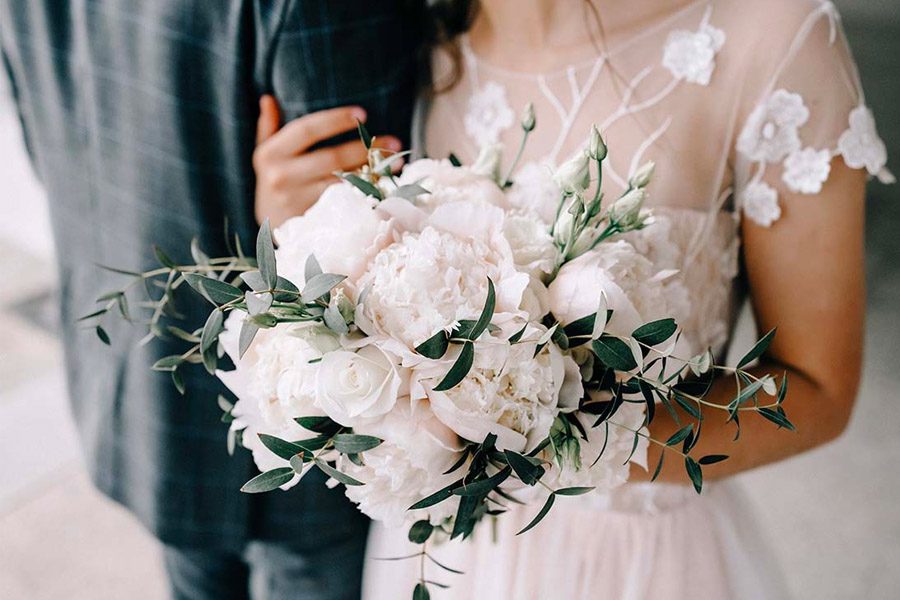 Wedding Insurance - Close-up of a Bouquet in a Bride’s Hands While She is Holding the Arm of the Groom After the Wedding Ceremony