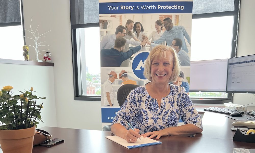 Celebrating Roxane Guzie – A Fond Farewell from Miers Insurance - Roxane Sitting at her desk smiling